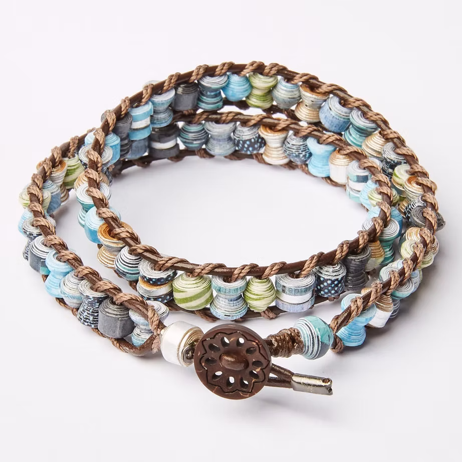 A handcrafted wrap bracelet with blue and cream paper beads and a bronze button