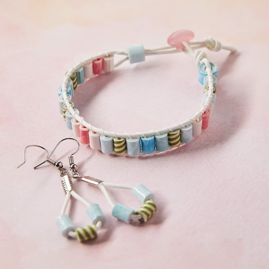 A pastel paper bead bracelet with matching earrings on a soft pink background